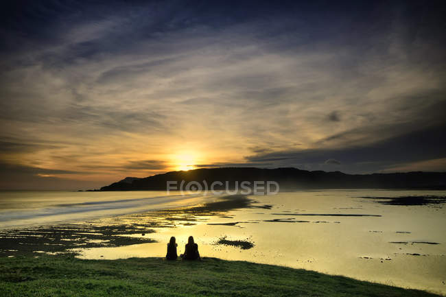 Indonesia, Lombok Island, silhouette of two women sitting at sunset over sea — Stock Photo
