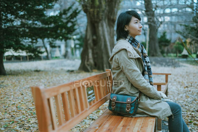 Vista lateral da bela mulher sentada no banco do parque — Fotografia de Stock