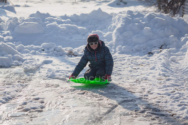 Мальчик зимой встает на колени на санях в снегу — стоковое фото