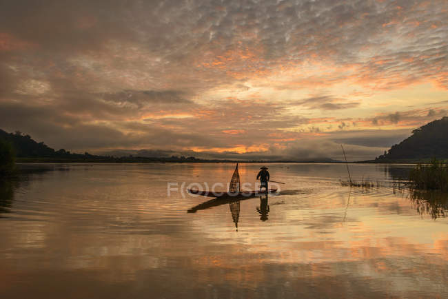 Человек, стоящий в рыбацкой лодке на закате, река Меконг, Таиланд — стоковое фото