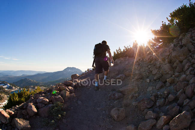 Hombre subiendo la montaña al atardecer, California, EE.UU. - foto de stock