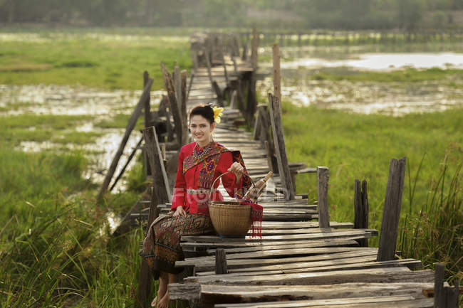 Портрет жінки в традиційному тайському одязі, що сидить на мосту — стокове фото
