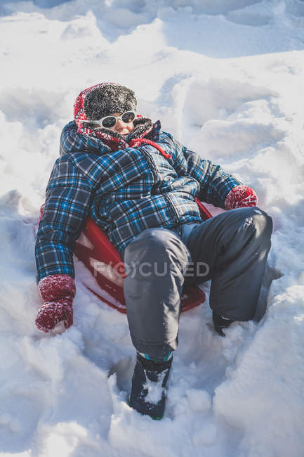 Хлопчик сидить на санях у снігу взимку — стокове фото