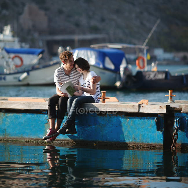 Bonito casal adolescente sentado no molhe abraçando — Fotografia de Stock