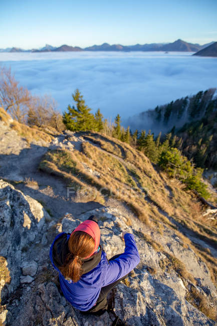 Frau auf dem Berg sitzend und Blick über Wolken, salzburg, Österreich — Stockfoto