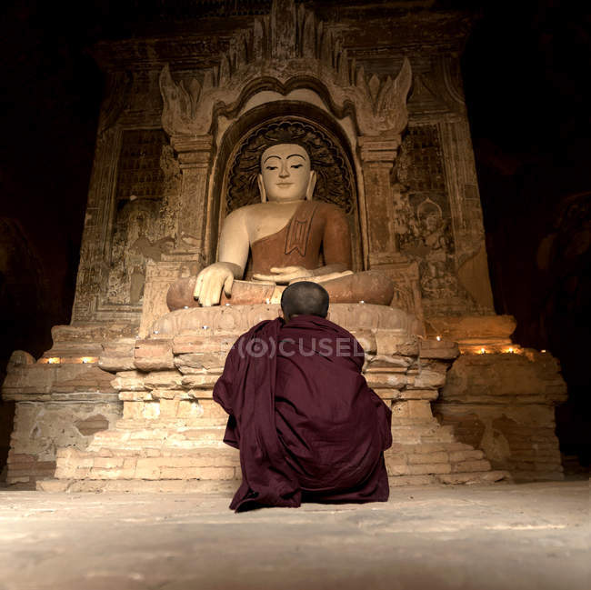 Monje novato sentado frente a la estatua de Buda en pagoda bagan, Mandalay, Myanmar - foto de stock