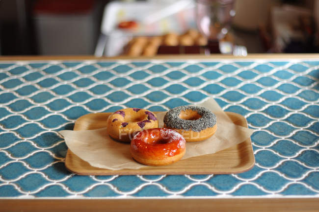 Three tasty donuts on baking paper on wooden tray — Stock Photo