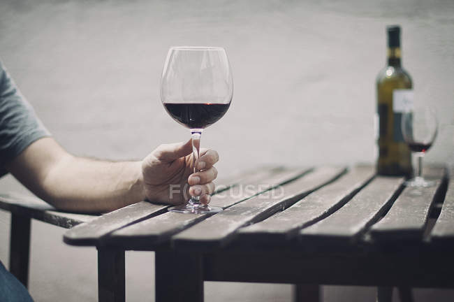 Imagem cortada do homem segurando vidro de vinho tinto sobre mesa de madeira ao ar livre — Fotografia de Stock
