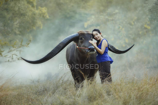 Mulher sorridente com os olhos fechados acariciando búfalo, Tailândia — Fotografia de Stock