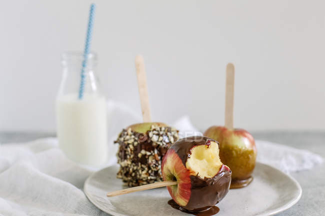 Шоколад и ириски яблоки на палочках с бутылкой молока — стоковое фото
