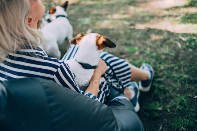 Блондинка в платье сидит на траве с двумя собаками в солнечный день — стоковое фото
