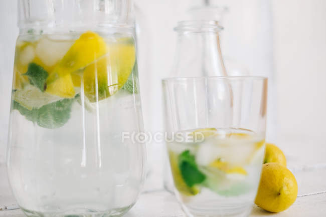 Copo e jarro de água com limão fresco, limão, hortelã e cubos de gelo — Fotografia de Stock