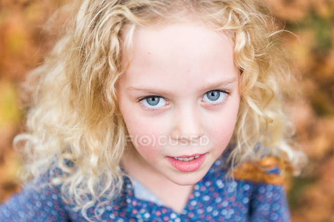 Blond little girl with blue eyes standing in autumn leaves — Stock Photo