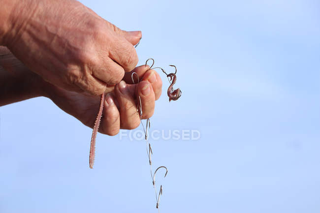 Primeros planos de las manos de la mujer Poner cebo en el anzuelo de pesca contra el cielo azul - foto de stock