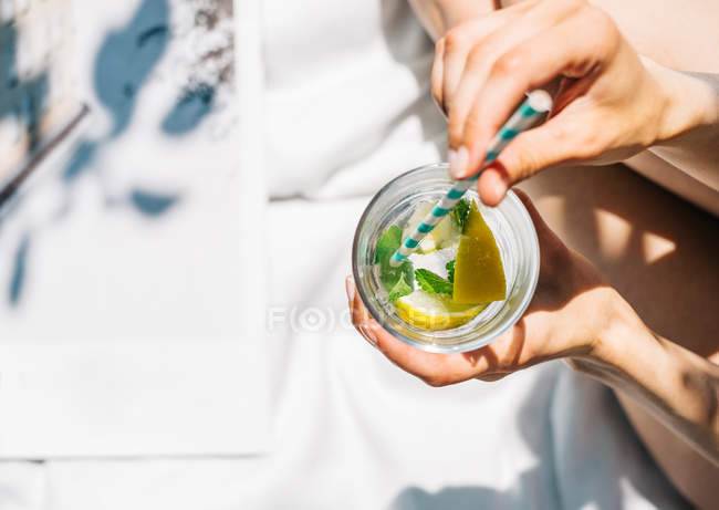 Female hands holding lemon cocktail with colored straw — Stock Photo