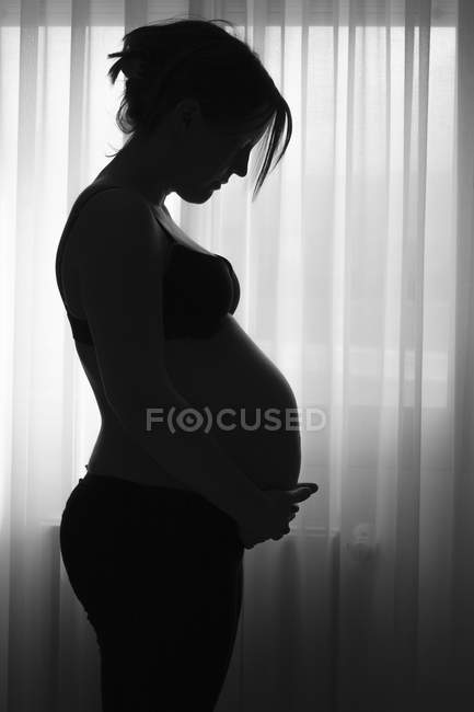 Silhouette einer schwangeren Frau, die zu Hause steht und den Bauch hält — Stockfoto