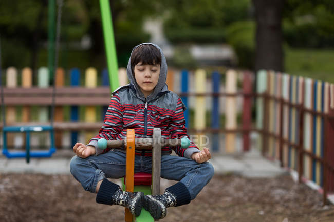 Мальчик в капюшоне медитирует на детской площадке — стоковое фото