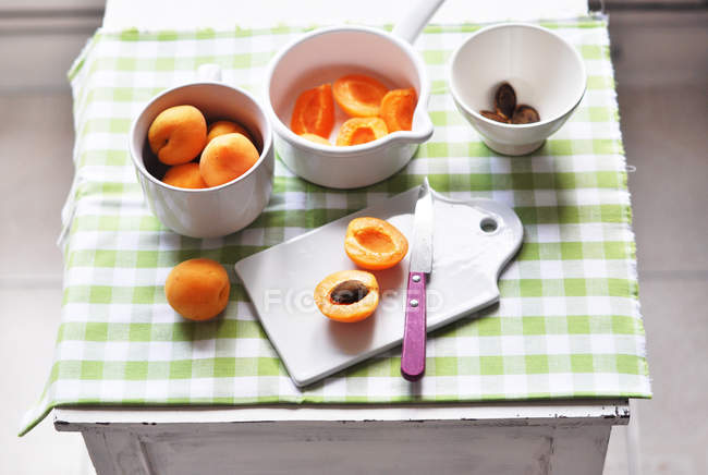 Albicocche fresche intere e dimezzate su un tavolo da cucina — Foto stock