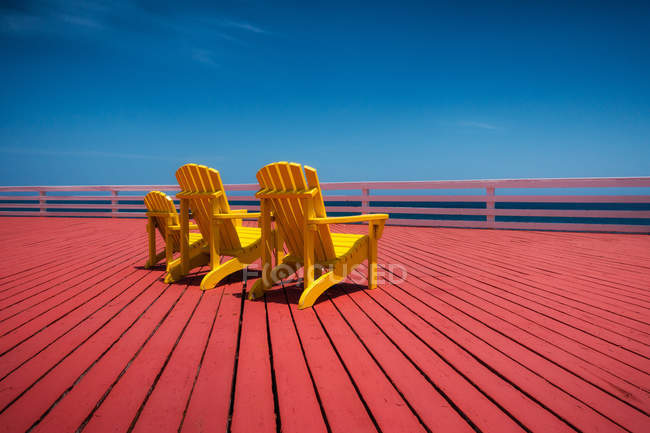 Três cadeiras amarelas no convés de madeira vermelho — Fotografia de Stock