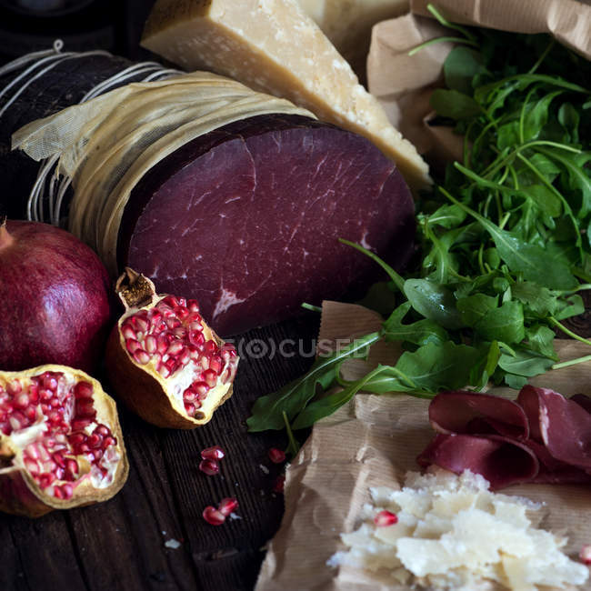 Bresaola and pomegranate fruits on wooden table — Stock Photo