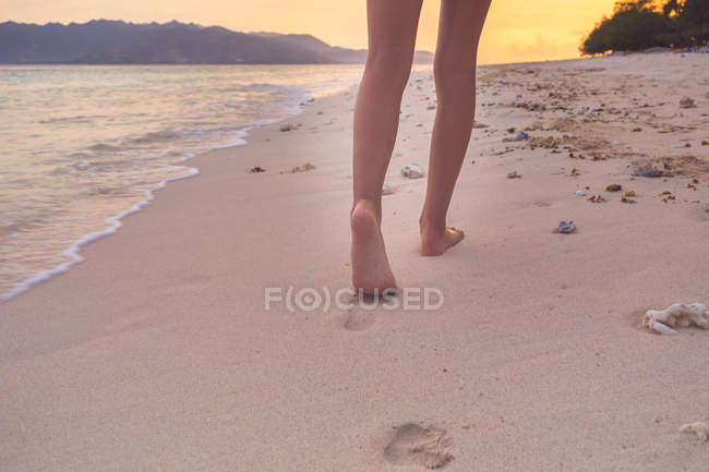 Обрезанное изображение ноги девушки, идущей по пляжу, вид сзади — стоковое фото