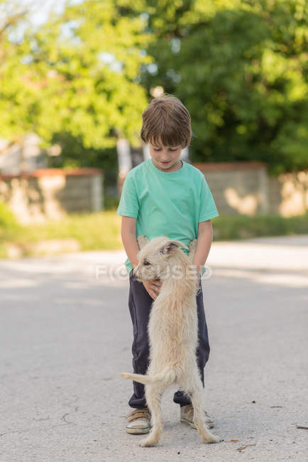 Хлопчик грає з білим собаку на вулиці — стокове фото