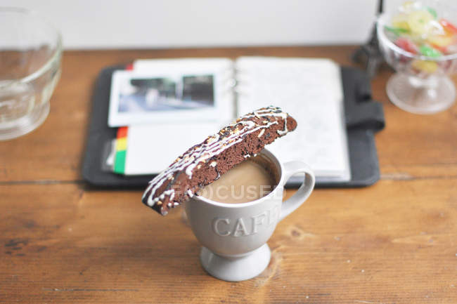 Cup of hot coffee with biscotti on table beside notebook — Stock Photo