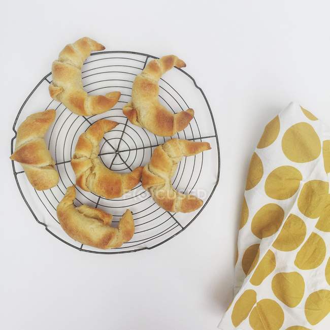 Croissants on metal cooling rack with tea towel — Stock Photo