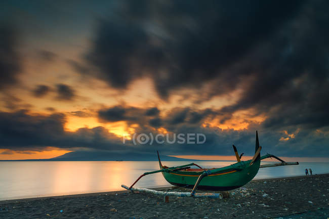 Indonesia, Banyuwangi, Santen Island, vista panorámica de la salida del sol en la playa con barco de pesca en primer plano - foto de stock