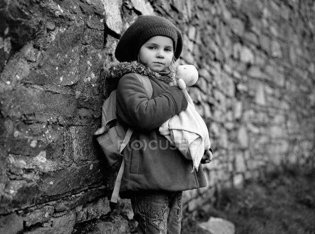 Girl holding teddy bear in front of brick wall — Stock Photo