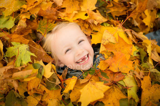 Lachen blondes kleines Mädchen mit Herbstblättern bedeckt — Stockfoto