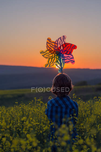 Junge hält bei Sonnenuntergang eine Spielzeugwindmühle in der Natur — Stockfoto