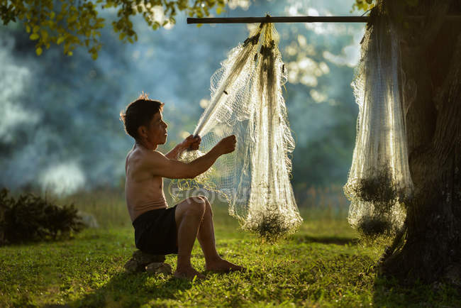 Pescador que classifica as redes de pesca penduradas na árvore ao pôr do sol — Fotografia de Stock