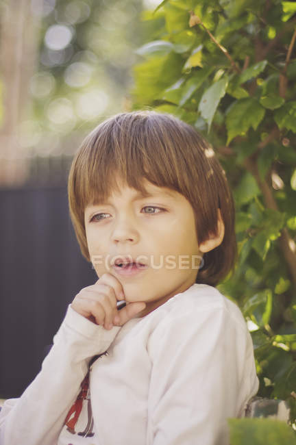 Menino pensando com a mão no queixo ao ar livre — Fotografia de Stock