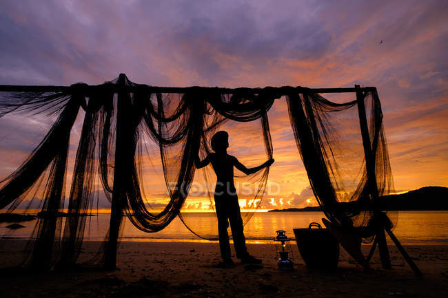 Silhouette eines Mannes, der am Strand bei Fischernetzen steht, Penang, Malaysia — Stockfoto