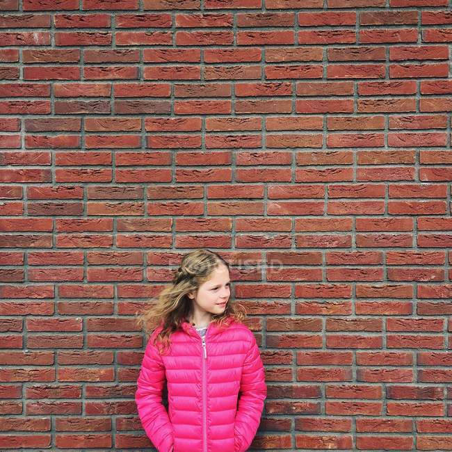 Портрет девушки в розовой куртке, стоящей напротив кирпичной стены — стоковое фото