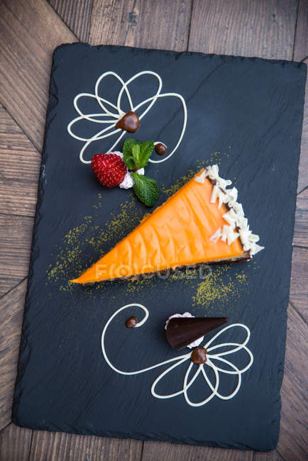 Вид зверху на шматочок торта на чорній дошці на дерев'яному фоні — стокове фото