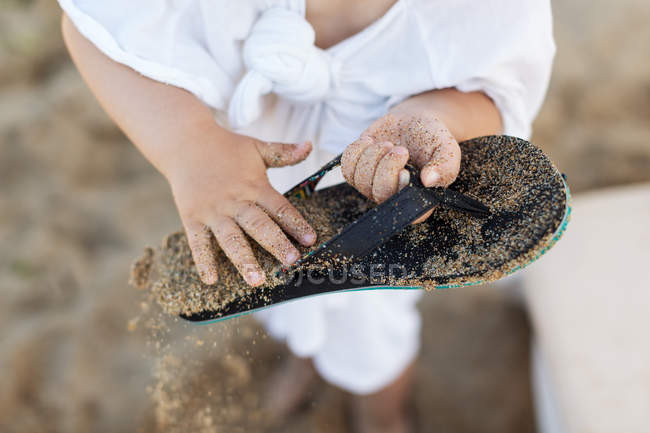 Крупним планом маленький хлопчик чистить пісок від фліп-флоп — стокове фото