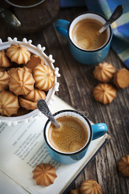 Kekse, Buch und Kaffeetassen über Holztisch — Stockfoto
