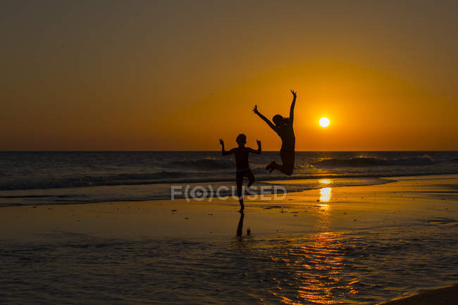 Силуэт мальчиков и девочек, прыгающих по пляжу — стоковое фото
