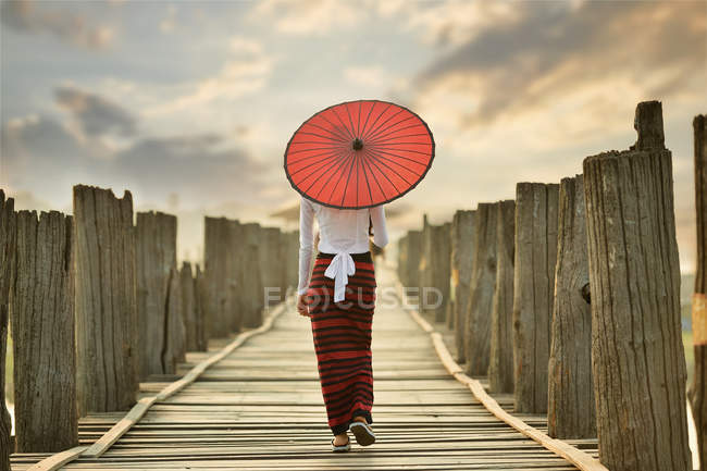 Beautiful young woman with red traditional umbrella standing on U Bein Bridge, Mandalay, Myanmar — Stock Photo