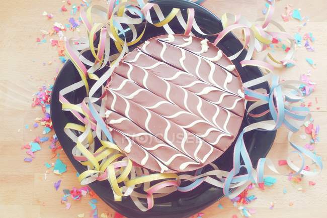 Chocolate cake surrounded by streamers and confetti — Stock Photo
