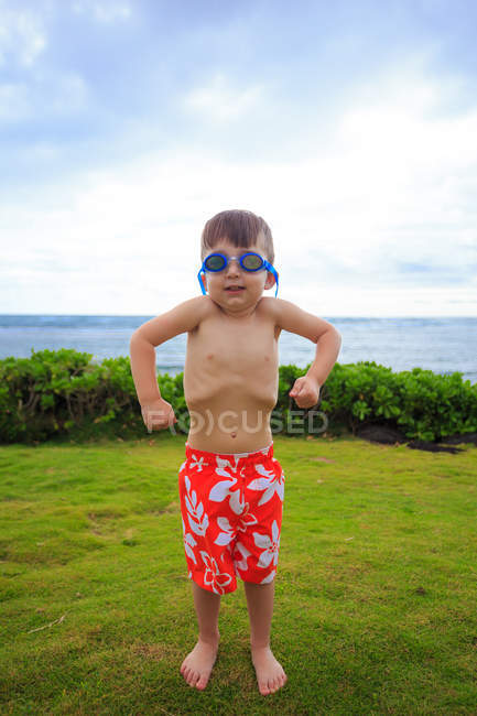 Little boy wearing goggles flexing muscles on lawn — Stock Photo