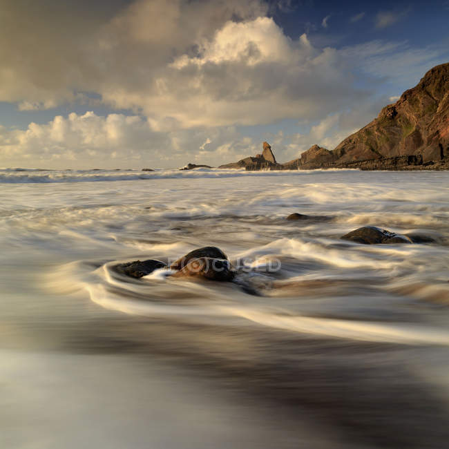 Довга експозиція морської мийки навколо каменів на пляжі — стокове фото
