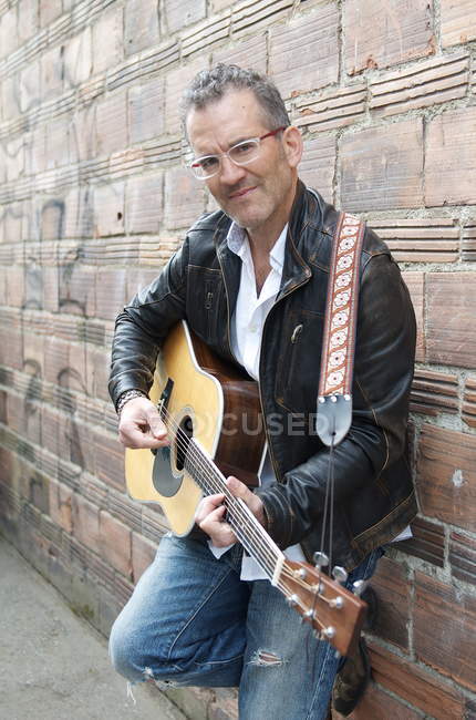 Портрет человека в переулке, играющего на гитаре и смотрящего в камеру — стоковое фото