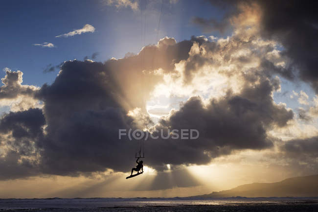 Silhouette of kite-surfer flying with cloudy sky on background at sunset — Stock Photo