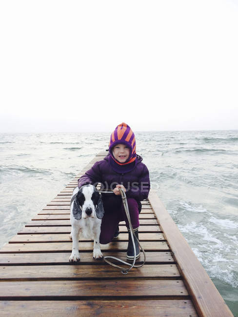 Ragazza con cane in piedi sul molo in riva al mare — Foto stock