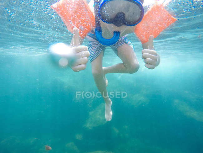 Хлопчик зі сноркліном, маскою та водяними крилами, що показують великі пальці в океані — стокове фото