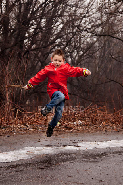 Ragazzo che indossa giacca rossa saltando sulla strada in inverno — Foto stock