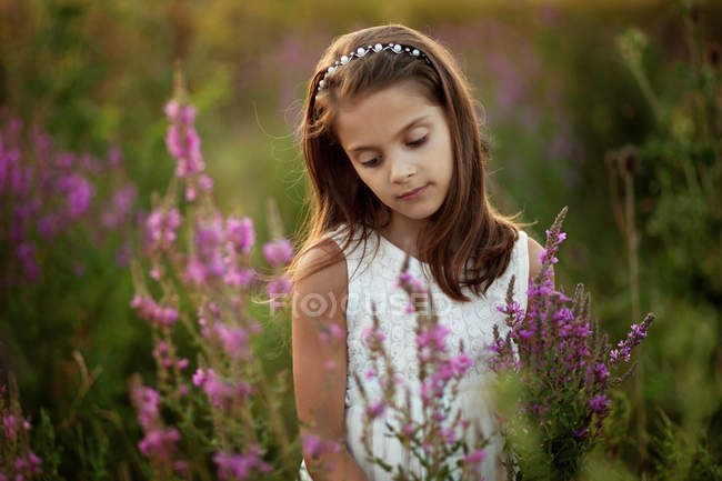 Portrait of girl standing in meadow between flowers — Stock Photo